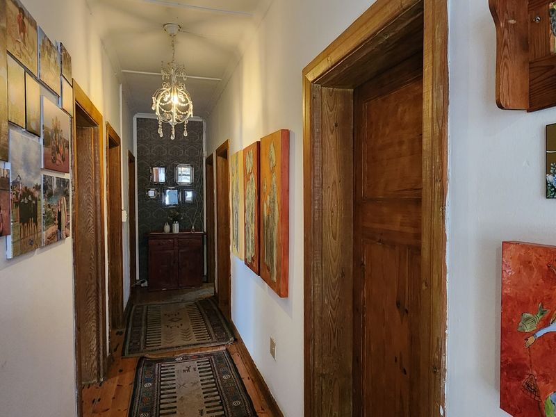 A well-lit hallway featuring hardwood flooring, classic wooden door frames, and a decorative chandelier, leading to a rear feature wall.