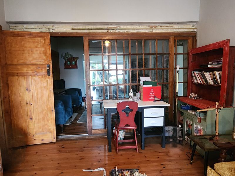 Living area featuring original timber flooring and large timber-framed sliding doors leading to an adjacent room, with some cosmetic finishing required.