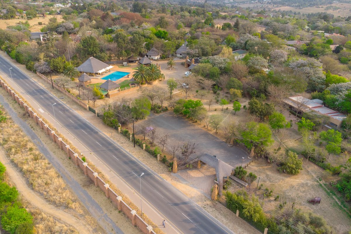 Aerial view of the guest house property featuring a swimming pool, multiple thatched roof buildings, extensive grounds, and a secure gated entrance.