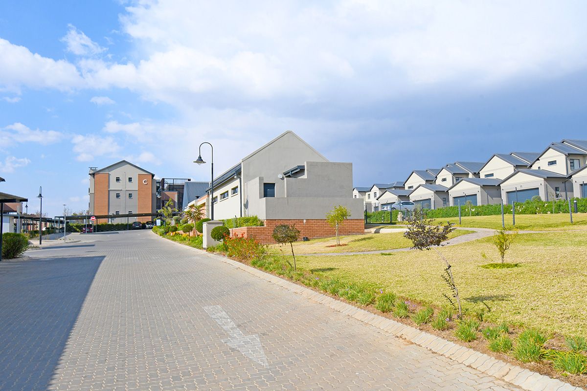 A view of the apartment complex grounds featuring paved driveways, landscaped lawns, and modern residential buildings with pitched roofs.