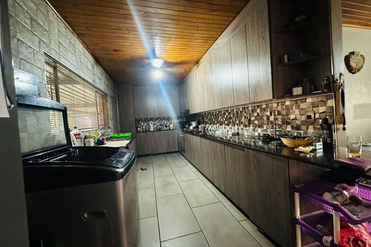 A galley-style kitchen featuring wood-look cabinetry, dark countertops, a mosaic tile backsplash, and a timber-paneled ceiling with tiled flooring.