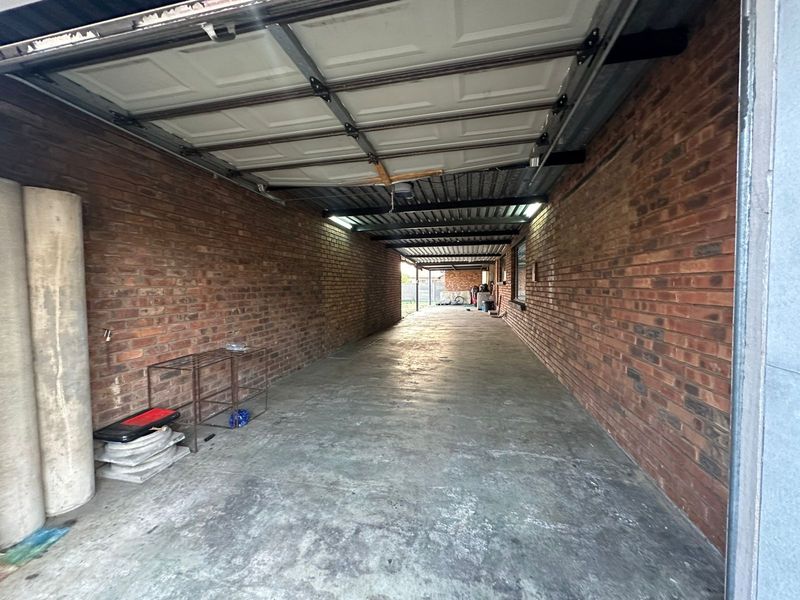 A long, covered tandem garage or carport featuring exposed brick walls, a concrete floor, and a sectional overhead garage door.