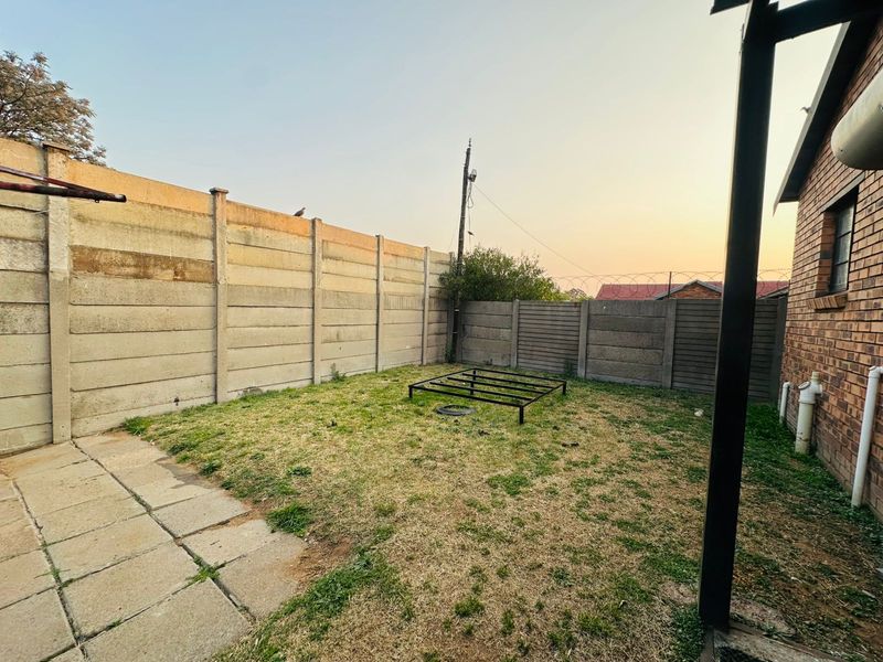A private rear garden area featuring a paved section, lawn, and high precast concrete boundary walls for added security.