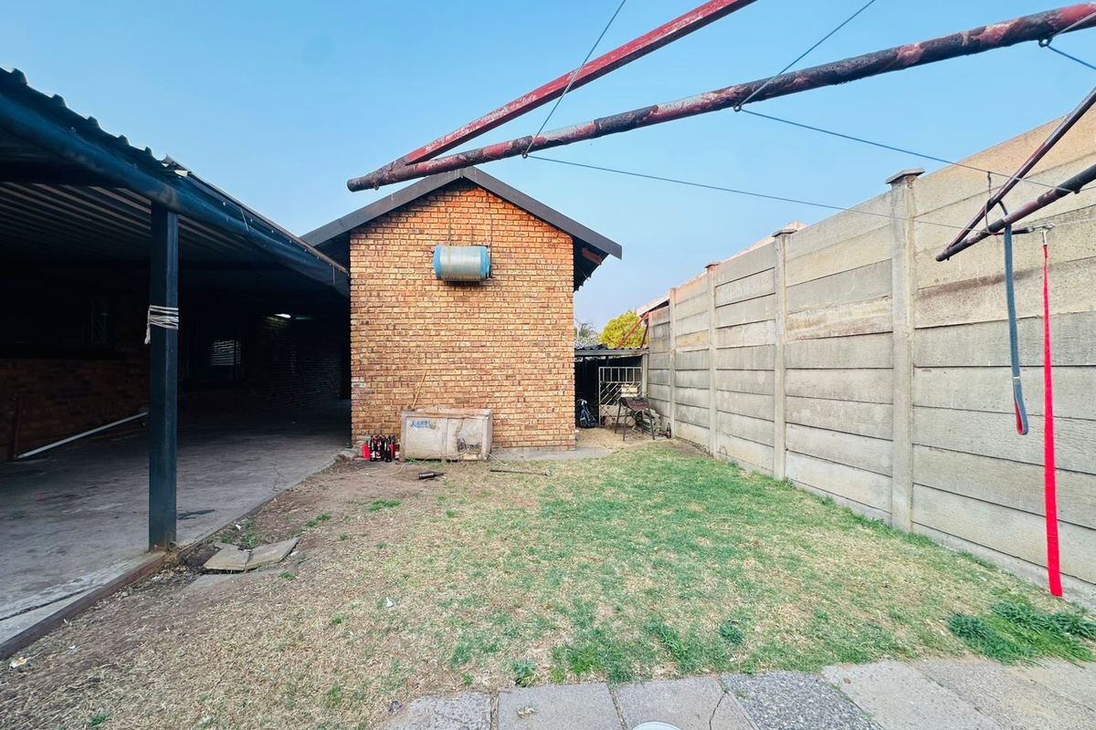 A rear exterior view of the property featuring a brick structure, a covered patio area, a small lawn, and concrete boundary walling.