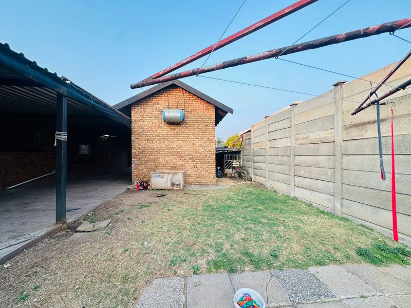 A rear exterior view of the property featuring a brick structure, a covered patio area, a small lawn, and concrete boundary walling.