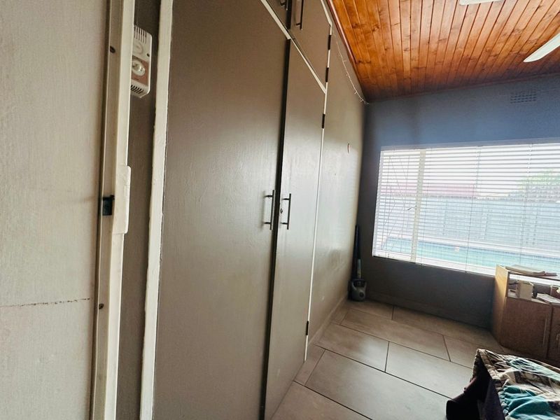 Bedroom featuring built-in cupboards, tiled flooring, and a timber-clad ceiling with a view of the pool area.