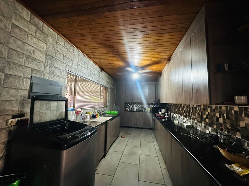 A galley-style kitchen featuring dark cabinetry, granite countertops, mosaic tile backsplash, and a timber-clad ceiling with integrated lighting.