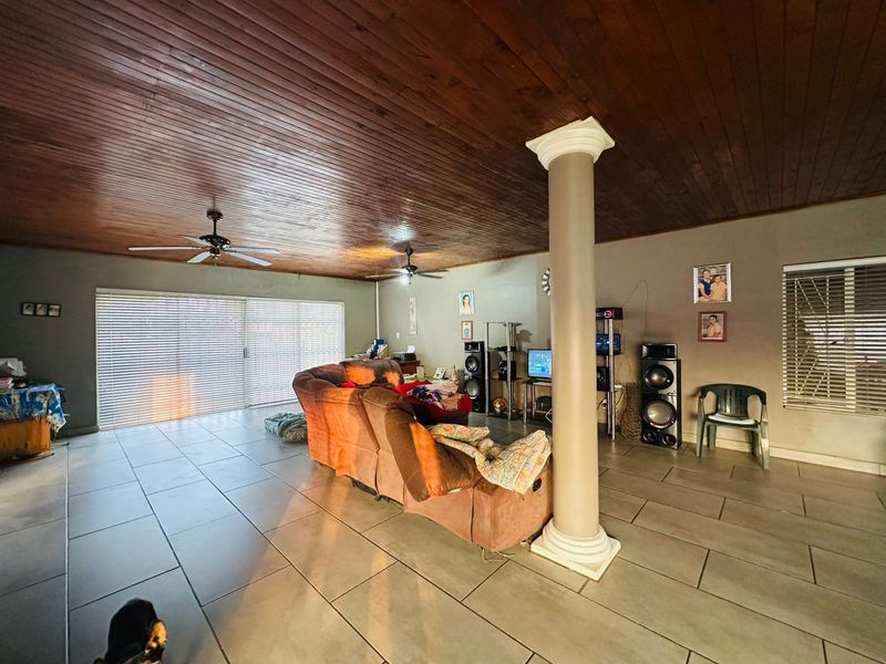 Spacious open-plan living area featuring a high timber-clad ceiling, tiled flooring, and a central structural column, with large sliding doors leading to the exterior.