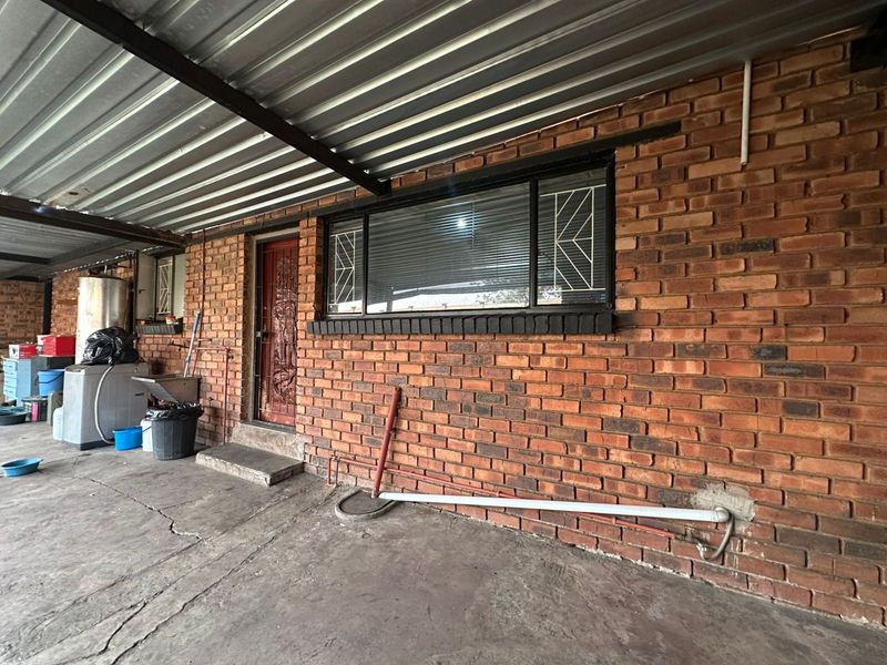 Covered outdoor utility area featuring exposed brick walls, corrugated metal roofing, and direct access to the home via a security door.