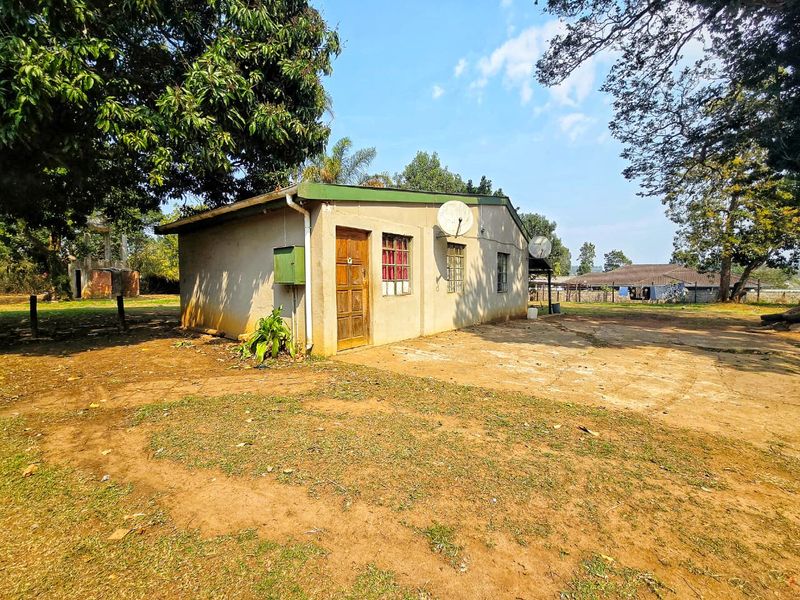 Rear view of a detached structure featuring a concrete apron, timber door, and steel window frames, set within a large, unlandscaped garden area.