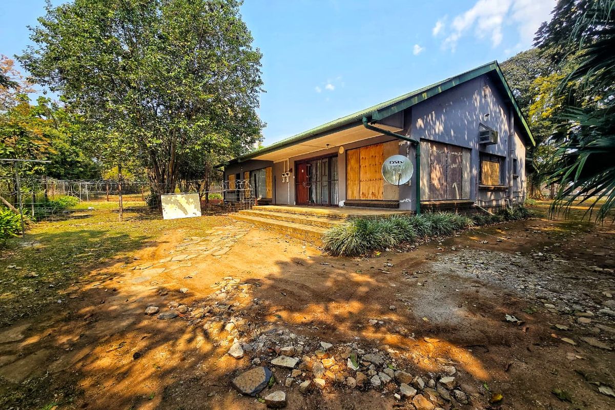 Rear view of a house showing significant exterior wear, boarded-up windows, and an unpaved yard area requiring maintenance and renovation.