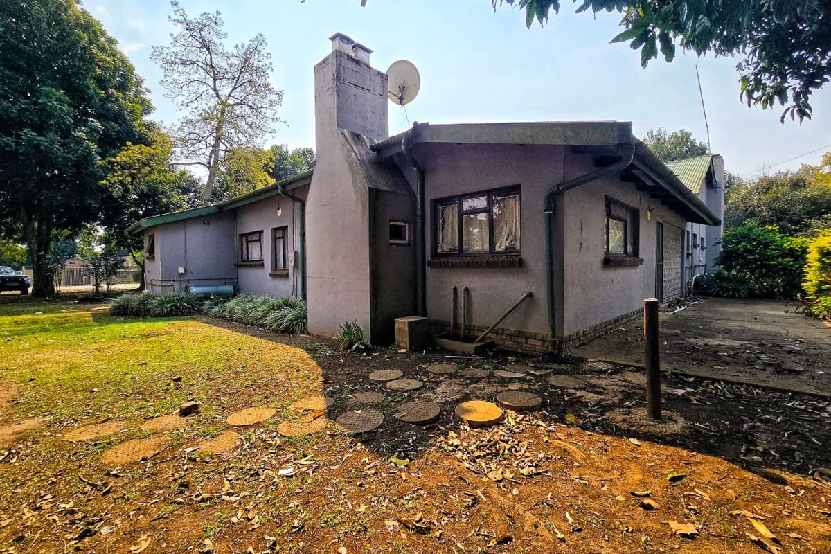 Rear view of the property featuring a prominent chimney, weathered plaster finish, and surrounding garden space with concrete paving.