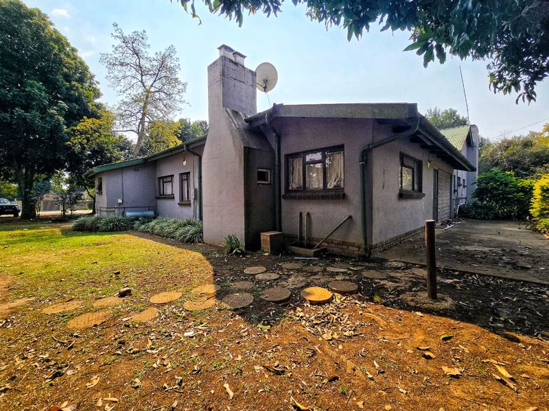 Rear view of the property featuring a prominent chimney, weathered plaster finish, and surrounding garden space with concrete paving.