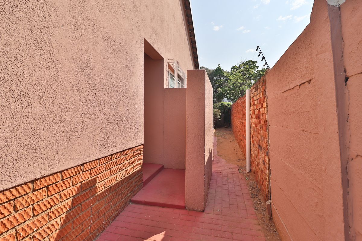 A side exterior walkway featuring a paved path, brick boundary wall with security spikes, and access to an external door.