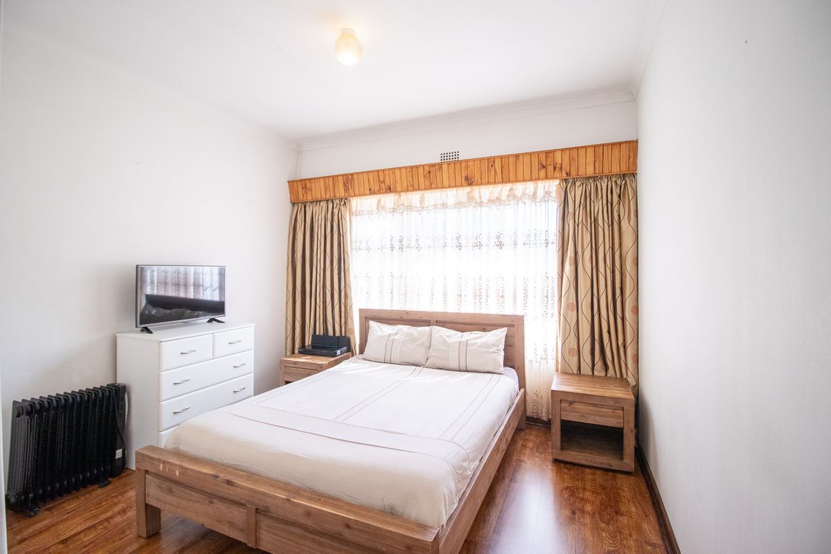 A bedroom featuring laminate flooring and a timber window pelmet, offering a functional space with natural light.