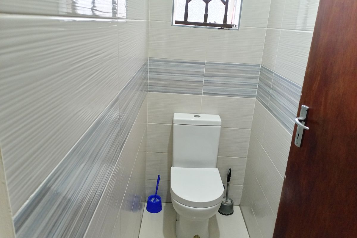 A compact, modern guest bathroom featuring tiled walls, a white ceramic toilet, and a small window with security bars.