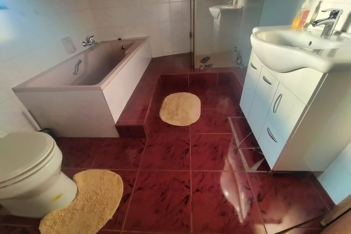 A dated bathroom featuring a built-in bathtub, vanity cabinet with basin, and toilet, finished with dark patterned floor tiles and white wall tiles.