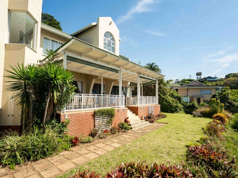 A well-maintained rear exterior view featuring a spacious covered patio, brick retaining wall, and a landscaped garden with a paved walkway.