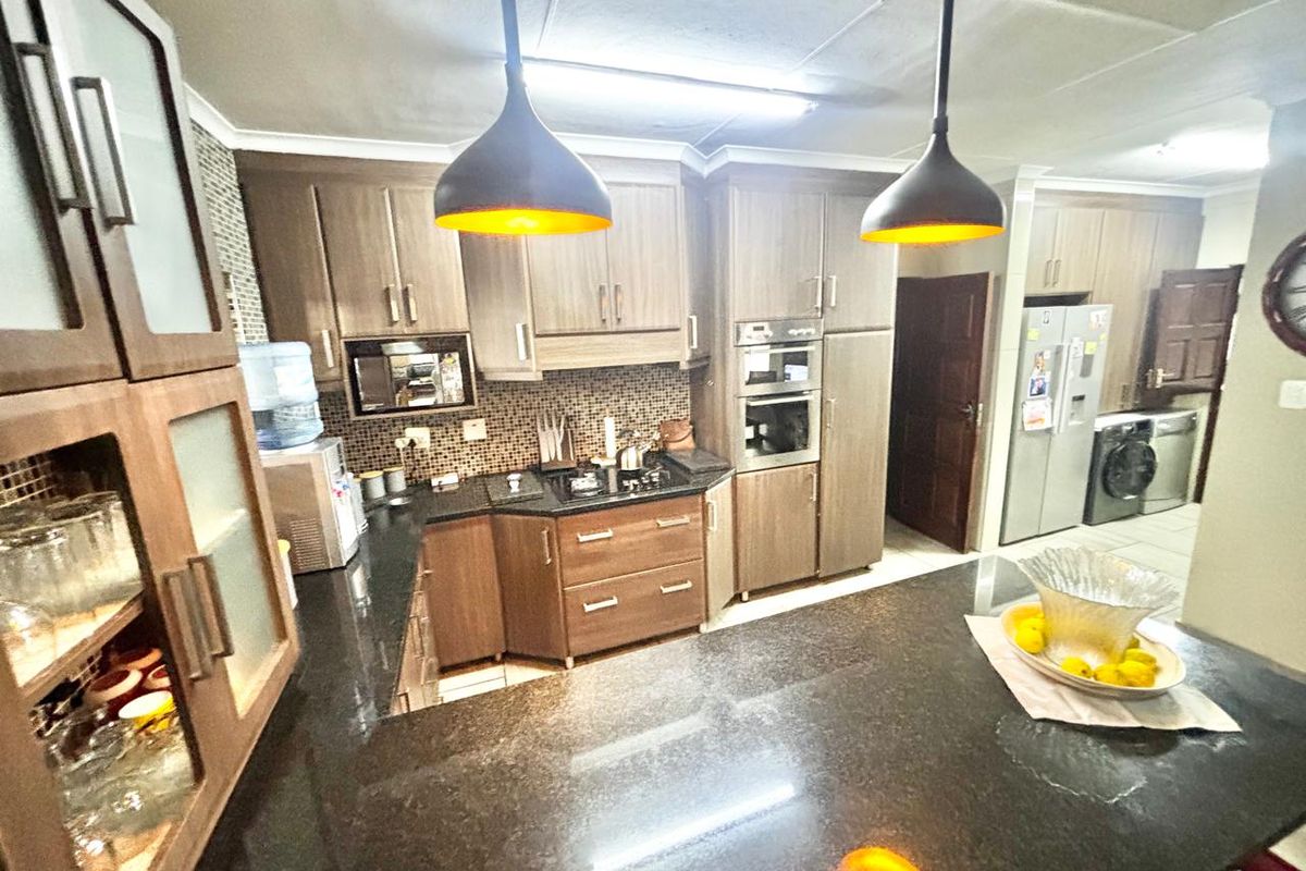 A functional kitchen featuring dark granite countertops, wood-finish cabinetry, built-in oven, and a mosaic tile backsplash with integrated pendant lighting.