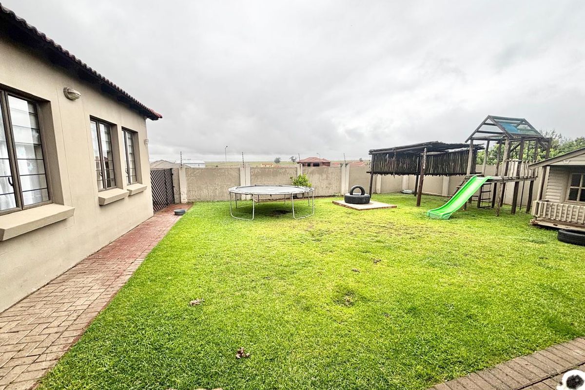 A spacious rear garden featuring a paved walkway, established lawn, and perimeter boundary walling.