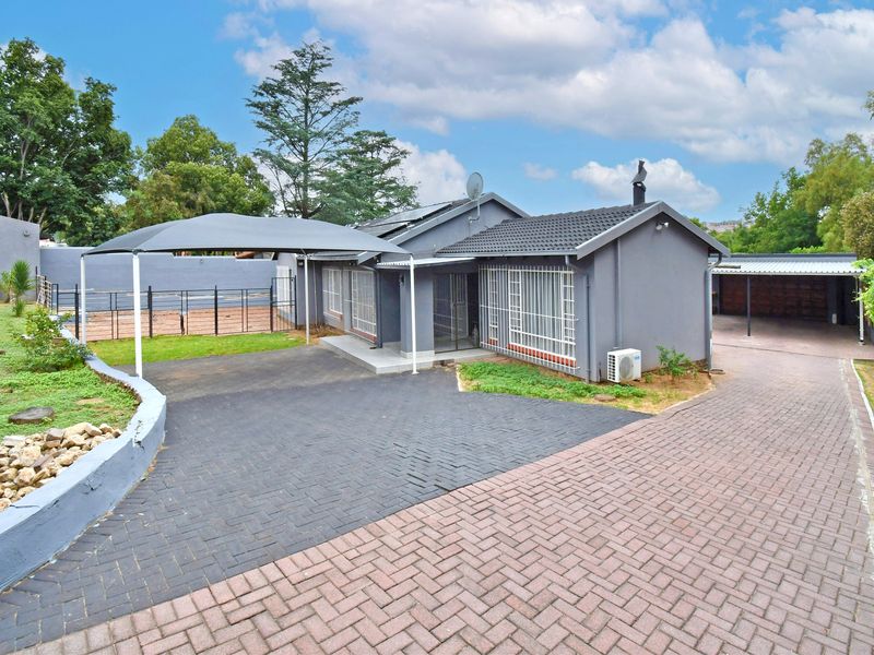 Front exterior view of the house featuring a paved driveway, carport, shade sail, and secure window bars.