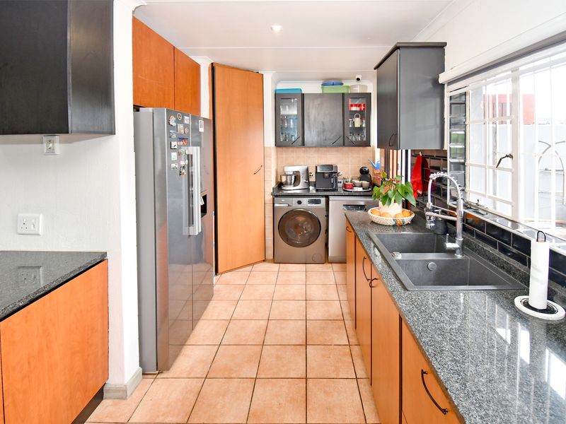 A functional kitchen featuring granite countertops, a double basin sink, tiled flooring, and a mix of wood-finish and dark cabinetry with integrated laundry space.