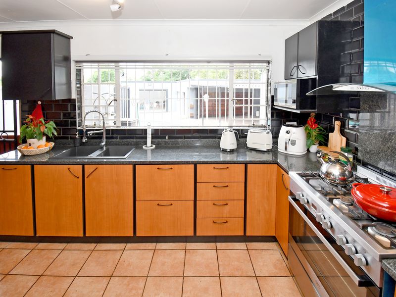 A functional kitchen featuring wood-finish cabinetry, granite countertops, a black subway tile backsplash, and a gas hob with an integrated extractor fan.