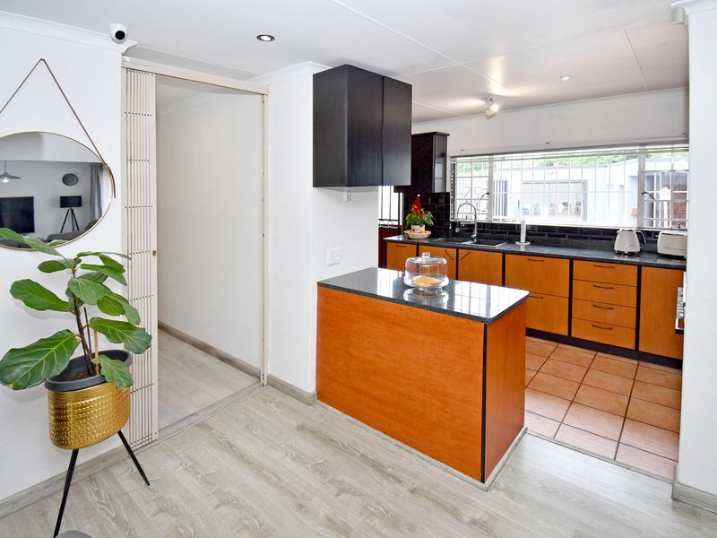 A functional kitchen featuring wooden cabinetry, a central island with a dark countertop, tiled flooring, and a window overlooking the exterior.