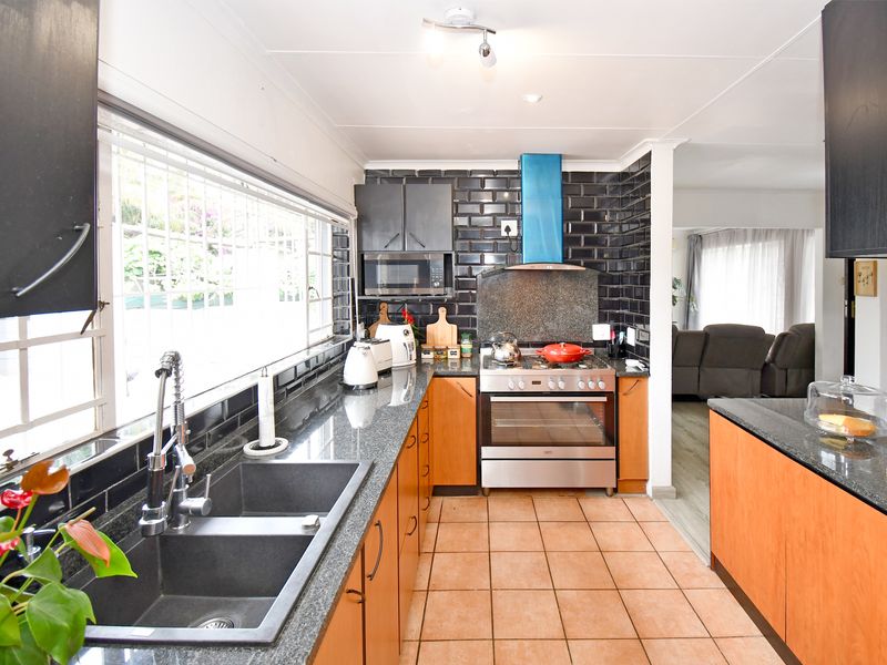 Modern kitchen featuring granite countertops, dark subway tile backsplash, stainless steel gas stove, and ample cabinetry, flowing into an adjacent living area.