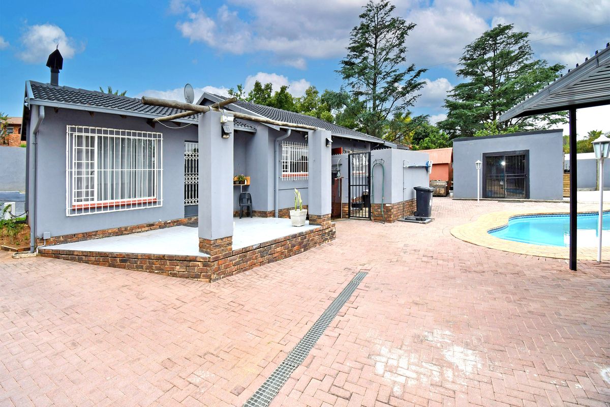 Rear exterior view featuring a paved patio area, swimming pool, and brick-accented building facade with security bars on windows.