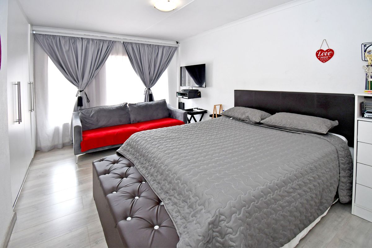 A well-maintained bedroom featuring light-toned laminate flooring, a built-in wardrobe, and large windows with curtain rails.
