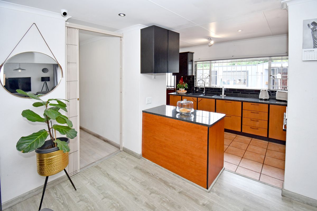 A functional kitchen featuring wooden cabinetry, a central island with a dark countertop, tiled flooring, and a window overlooking the exterior.