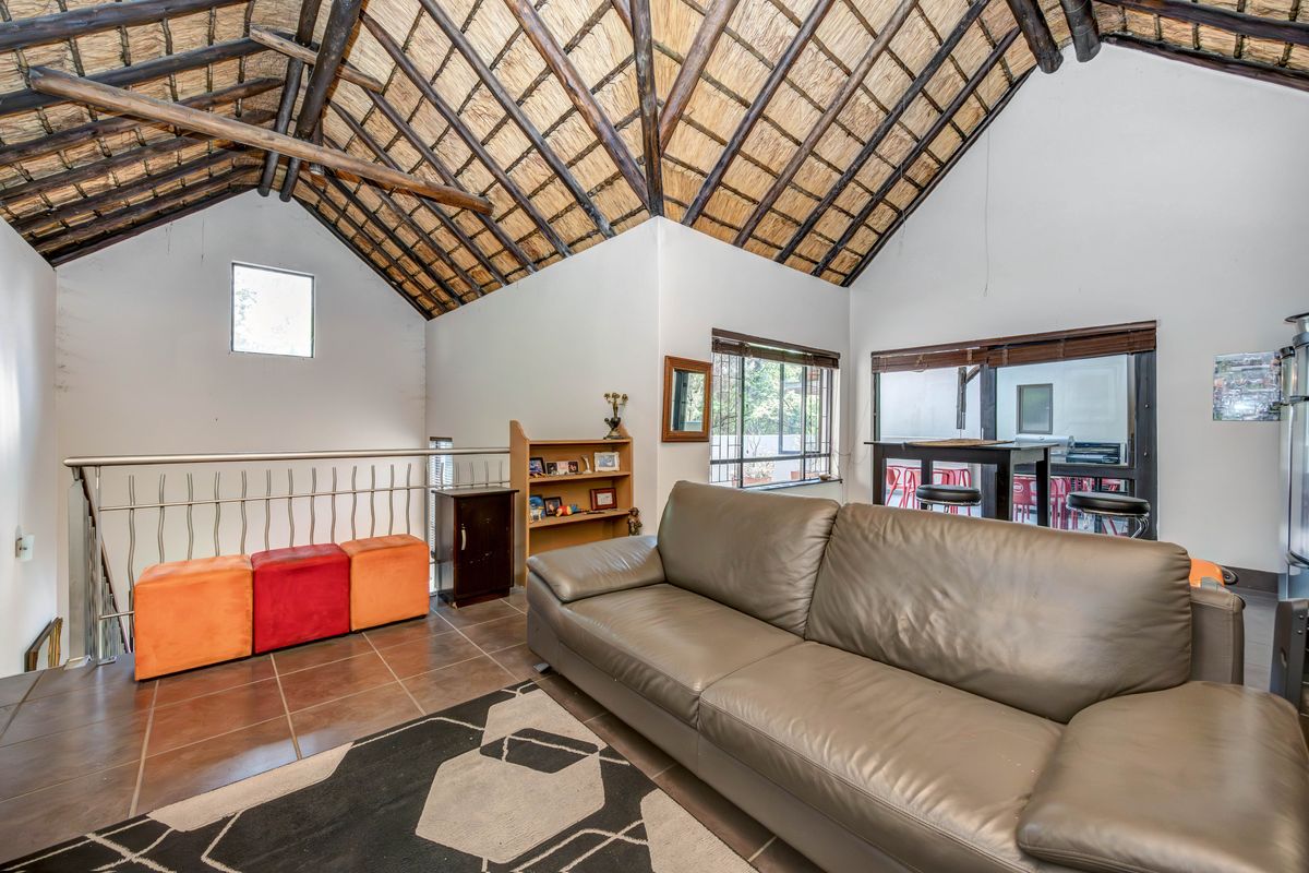 Spacious living area featuring a high vaulted thatched ceiling, tiled flooring, and a metal balustrade overlooking the lower level.