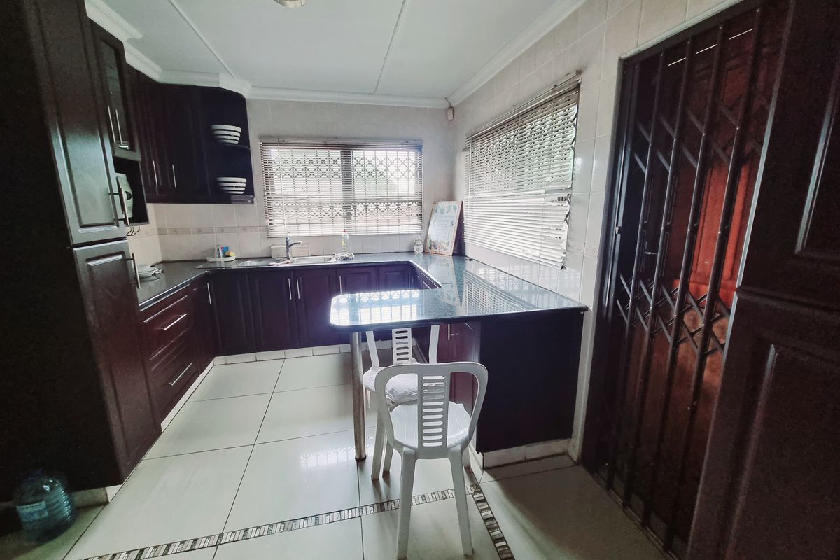 Functional kitchen featuring dark wood cabinetry, granite countertops, tiled flooring, and a breakfast nook area with security gate access.