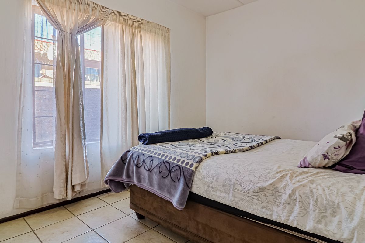 A functional bedroom featuring tiled flooring and natural light from a window with curtain fixtures.