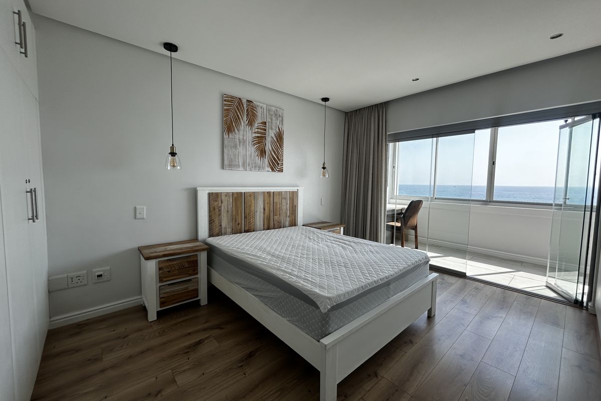 Modern bedroom featuring laminate flooring, built-in cupboards, and large sliding glass doors opening to a balcony with ocean views.