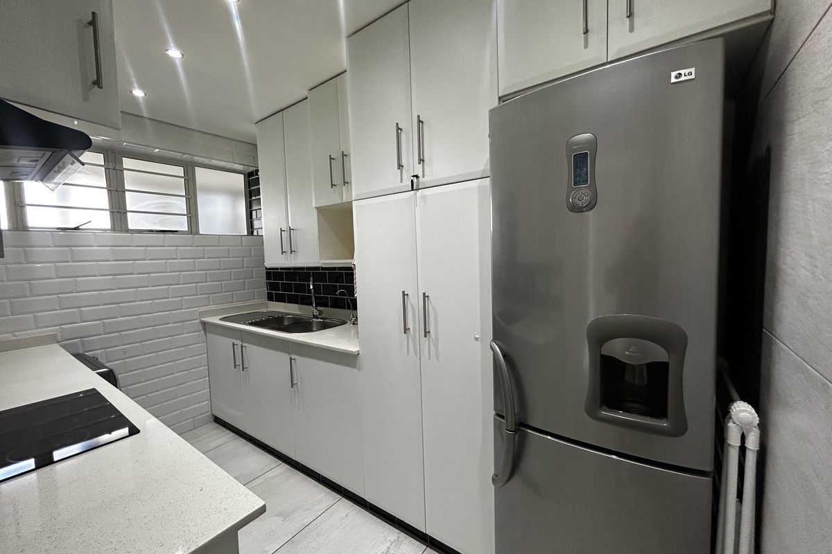 Modern kitchen featuring white cabinetry, stone countertops, subway tile backsplash, and integrated lighting, offering a clean and functional workspace.