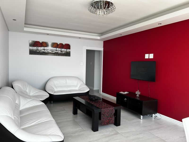 A living room featuring a bold red accent wall, recessed ceiling with downlights, and neutral tiled flooring.