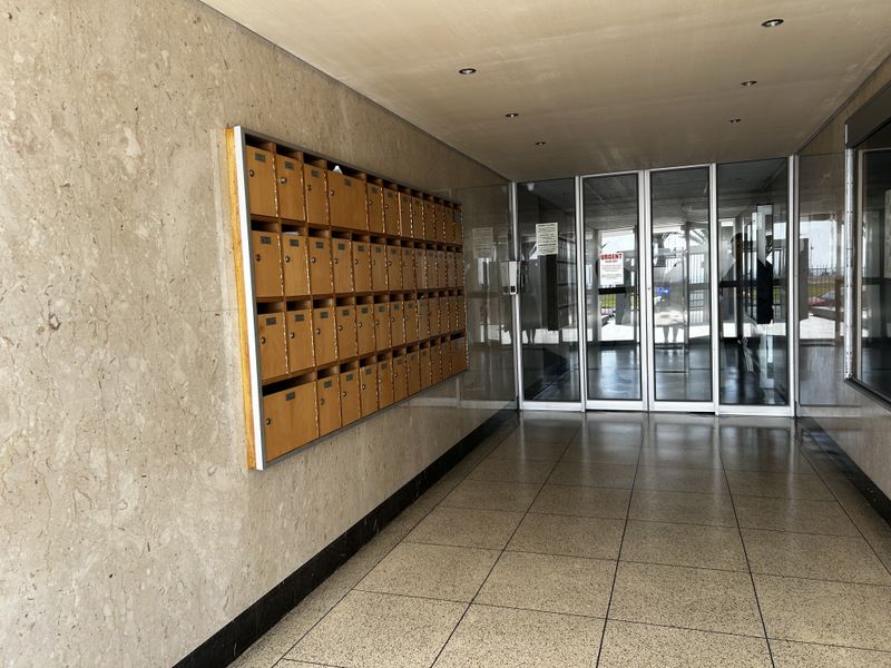 A clean and well-maintained apartment building entrance lobby featuring stone wall cladding, terrazzo flooring, and a wall-mounted bank of wooden mailboxes.