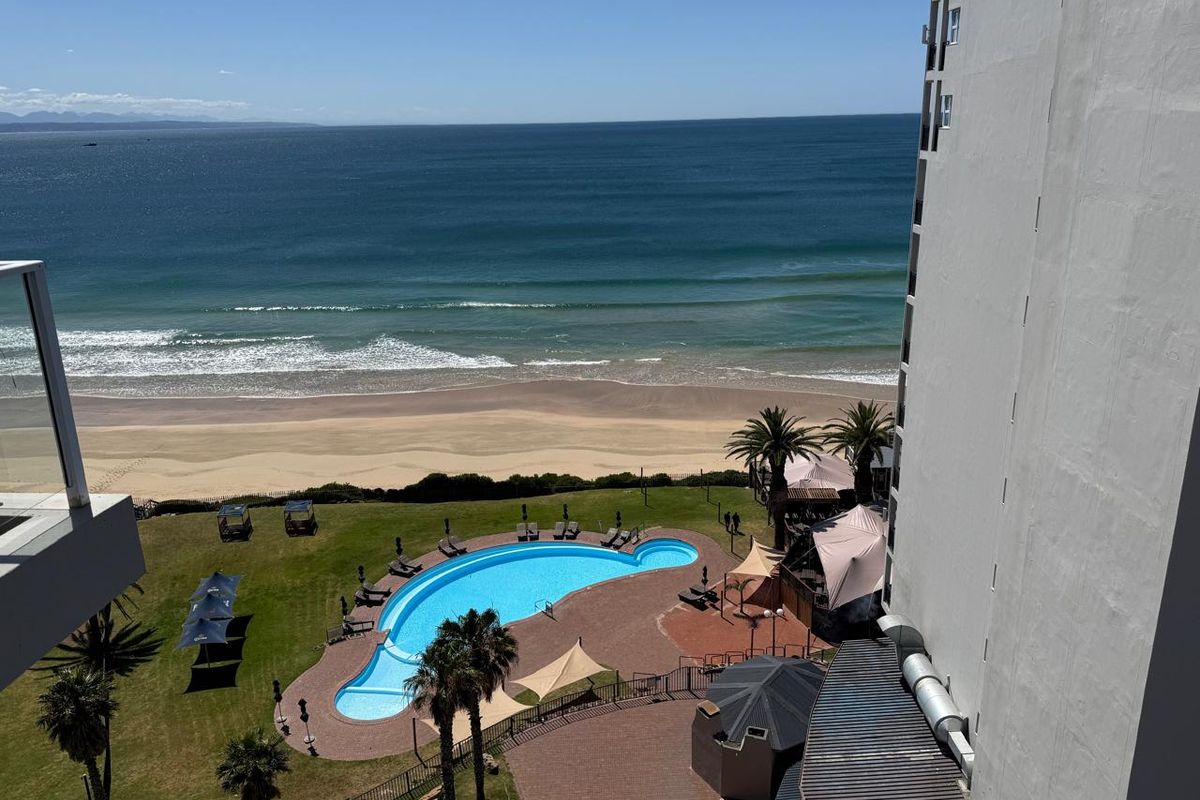 Elevated aerial view overlooking the communal swimming pool, landscaped garden area, and direct beach access from the apartment complex.