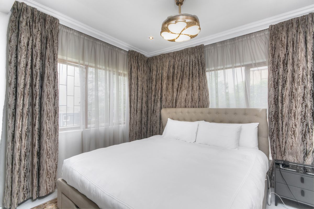 A well-lit bedroom featuring crown molding, large windows with integrated security bars, and a decorative ceiling light fixture.
