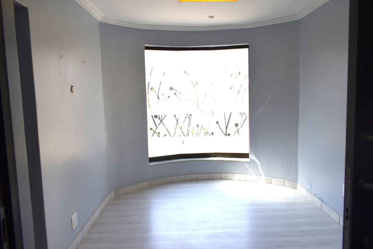 An empty bedroom featuring a curved bay window, light-toned laminate flooring, and neutral grey walls.
