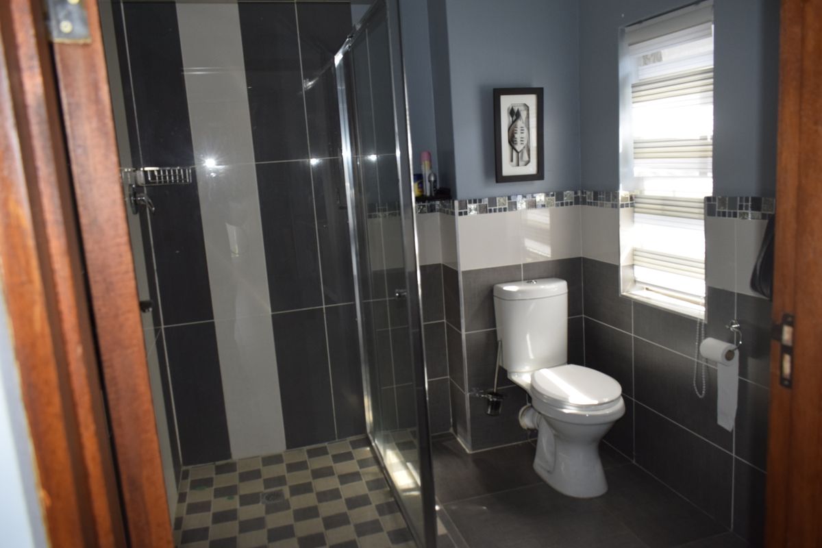 A modern bathroom featuring a glass-enclosed shower, tiled walls, and a standard toilet, finished with contemporary grey and white tiling.