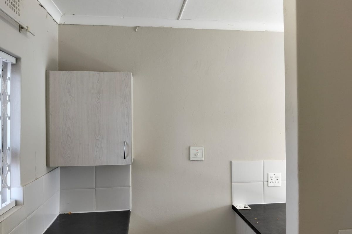 A compact kitchen area featuring laminate cabinetry, dark countertops, and tiled splashbacks, currently vacant and ready for renovation or modernization.
