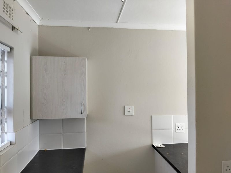 A compact kitchen area featuring laminate cabinetry, dark countertops, and tiled splashbacks, currently vacant and ready for renovation or modernization.