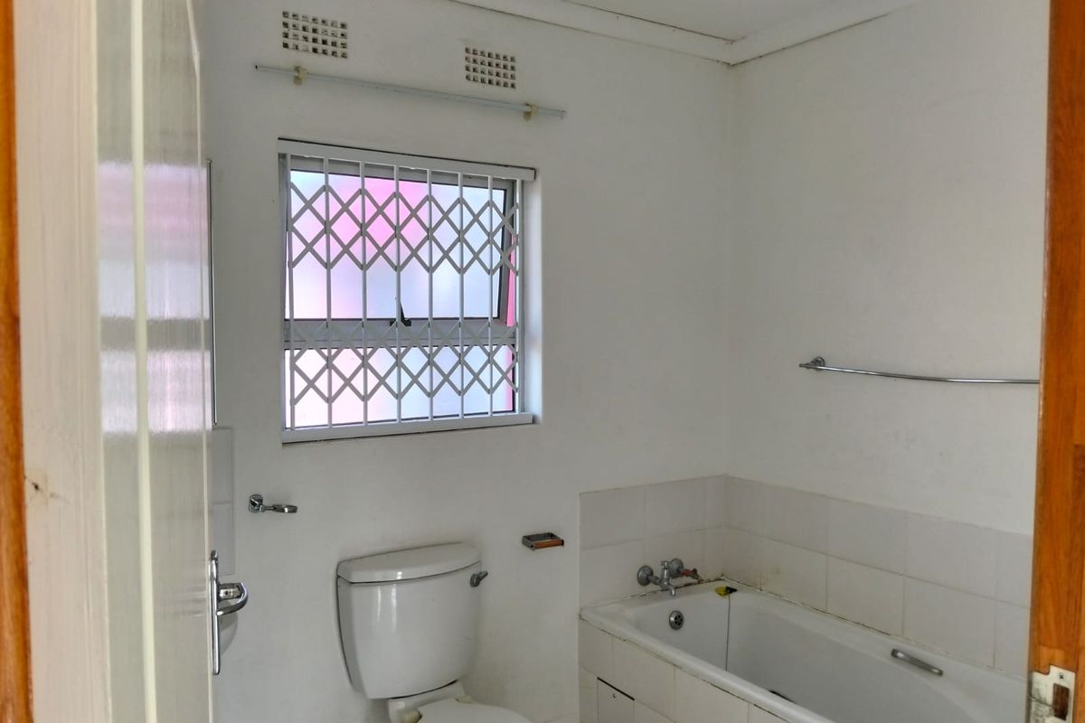 A functional bathroom featuring a standard bathtub, toilet, and security-fitted window, requiring cosmetic updates to improve its overall condition and appeal.