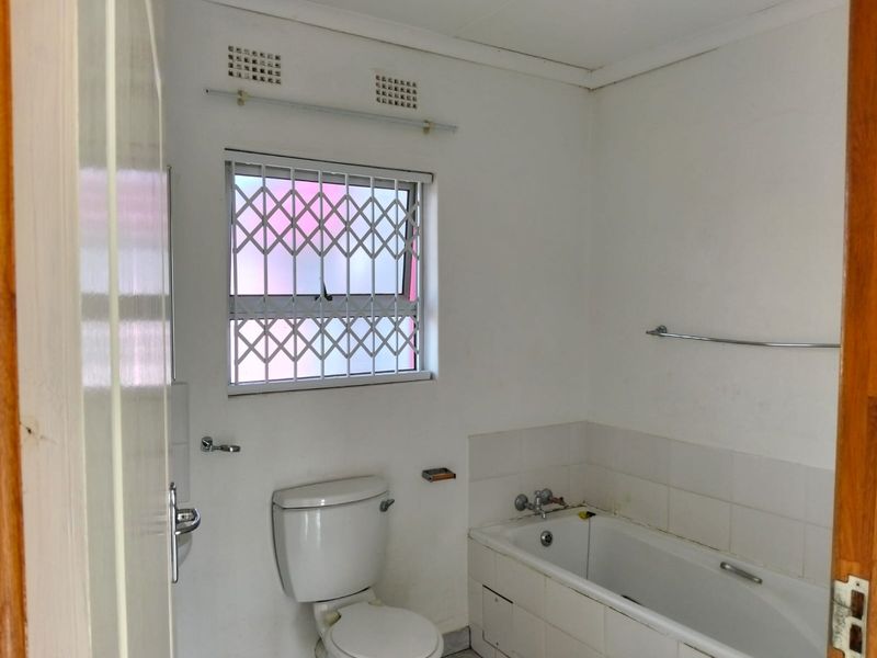 A functional bathroom featuring a standard bathtub, toilet, and security-fitted window, requiring cosmetic updates to improve its overall condition and appeal.