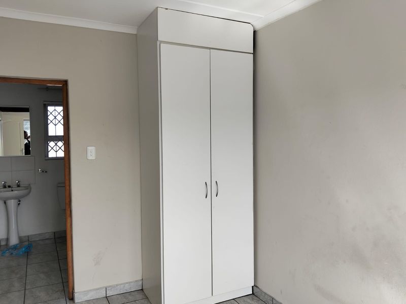 A bedroom featuring a white built-in wardrobe, tiled flooring, and neutral wall finishes, with an adjacent view into a bathroom.