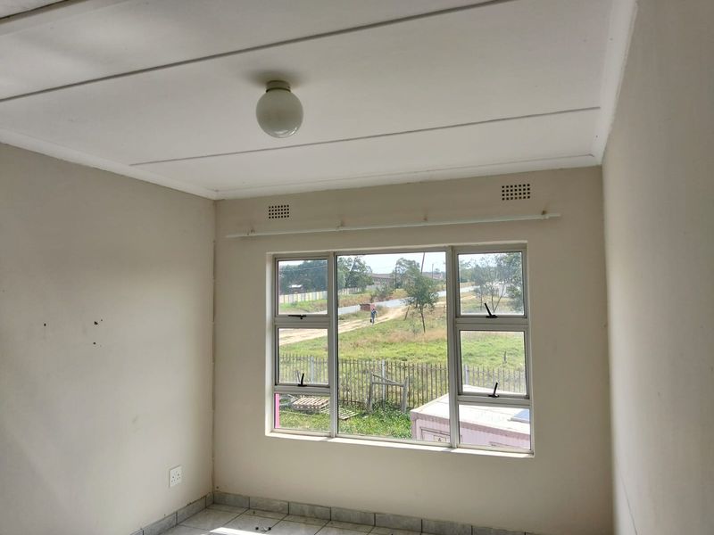 A bright, empty bedroom featuring tiled flooring, neutral walls, and aluminium-framed windows with a view of the surrounding area.