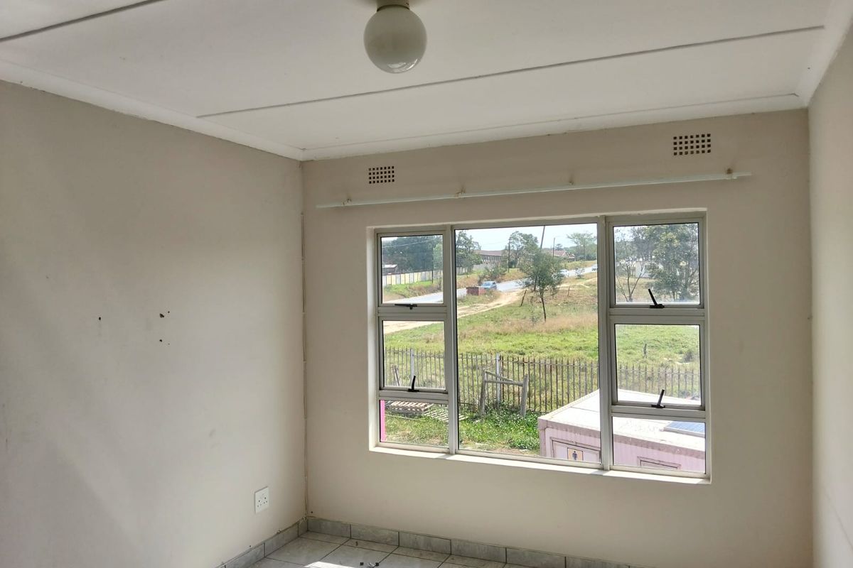 An empty bedroom featuring tiled flooring, neutral walls, and aluminium-framed windows with a view of the surrounding area.